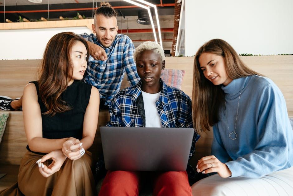 A diverse group of young professionals engaged in a collaborative project using a laptop in a modern office setting.
