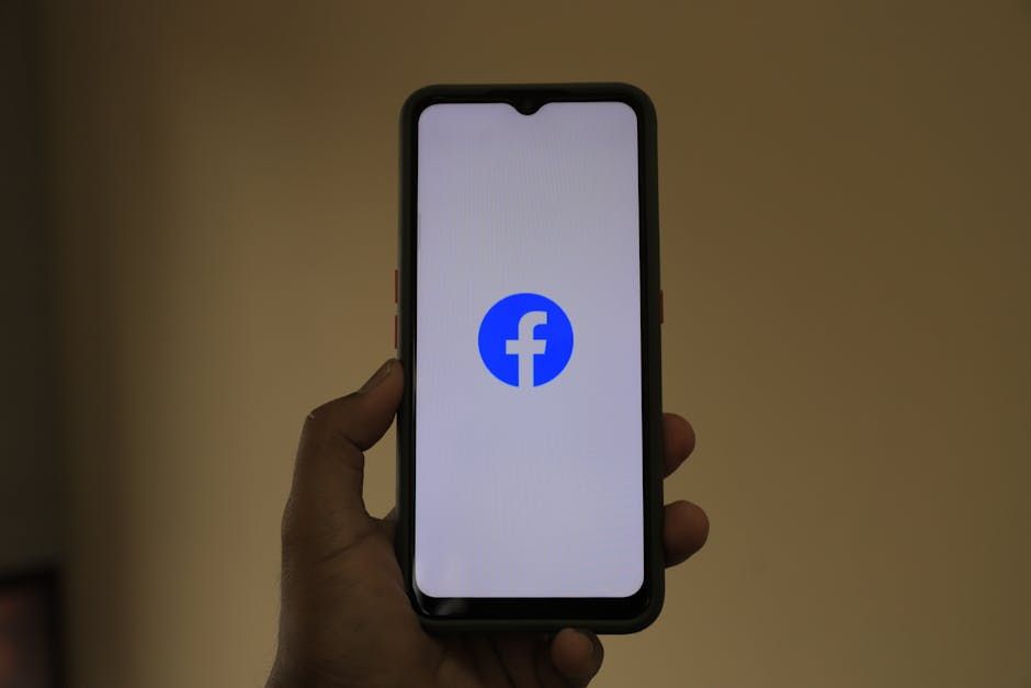 A smartphone held in hand showing the Facebook logo on its screen.