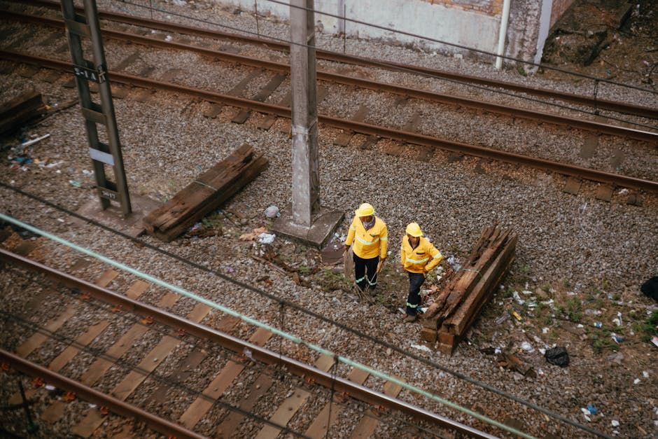 Two railway workers in yellow uniforms inspecting tracks, aerial view.