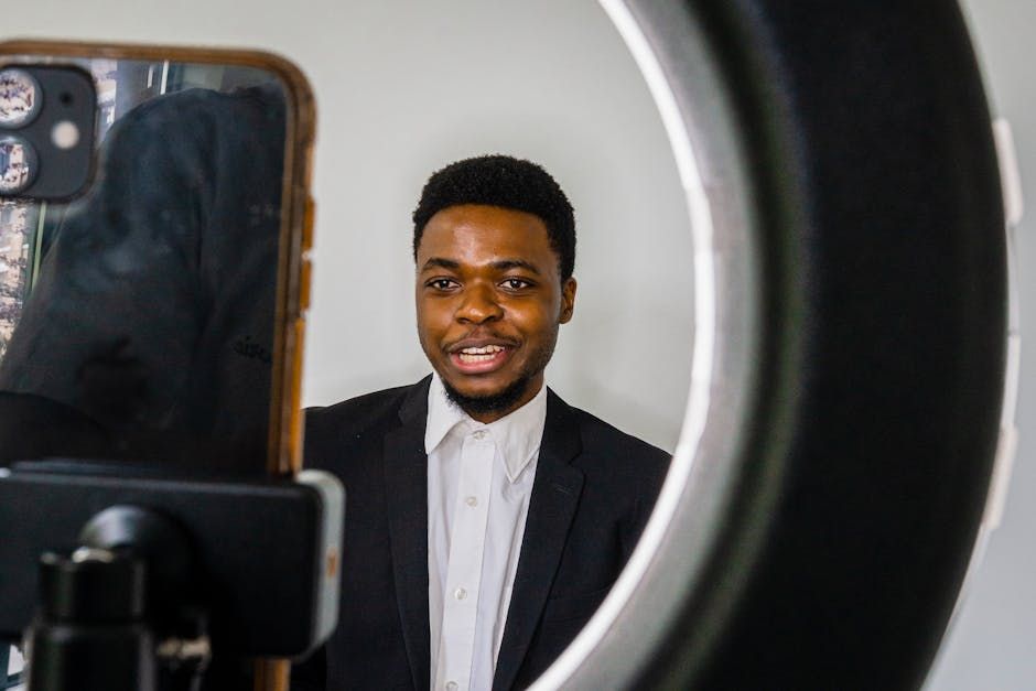 Young man in a blazer recording a vlog using a smartphone and a ring light.